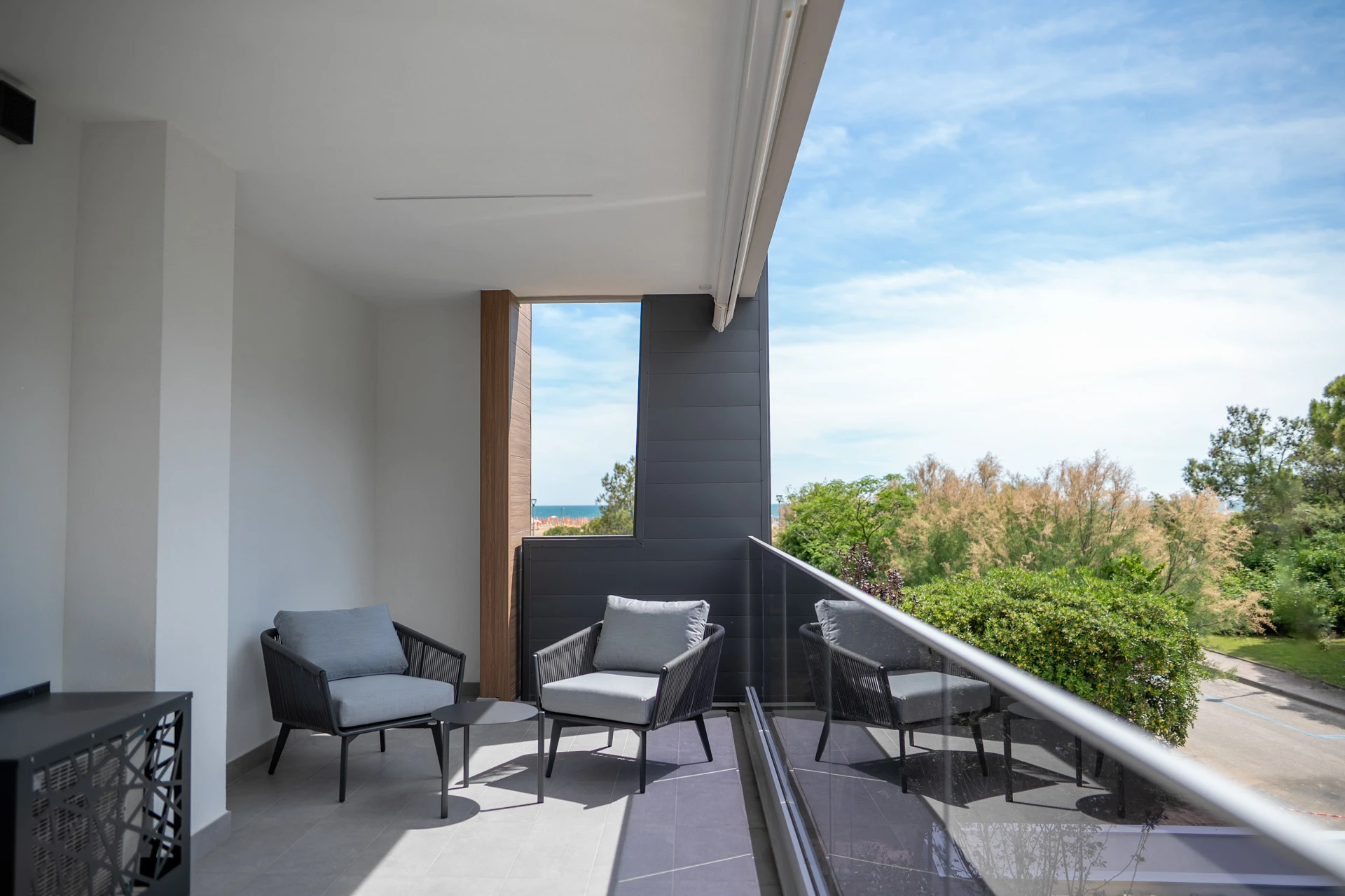 Balcone moderno con poltrone e tavolino, vista sul verde e scorcio di mare