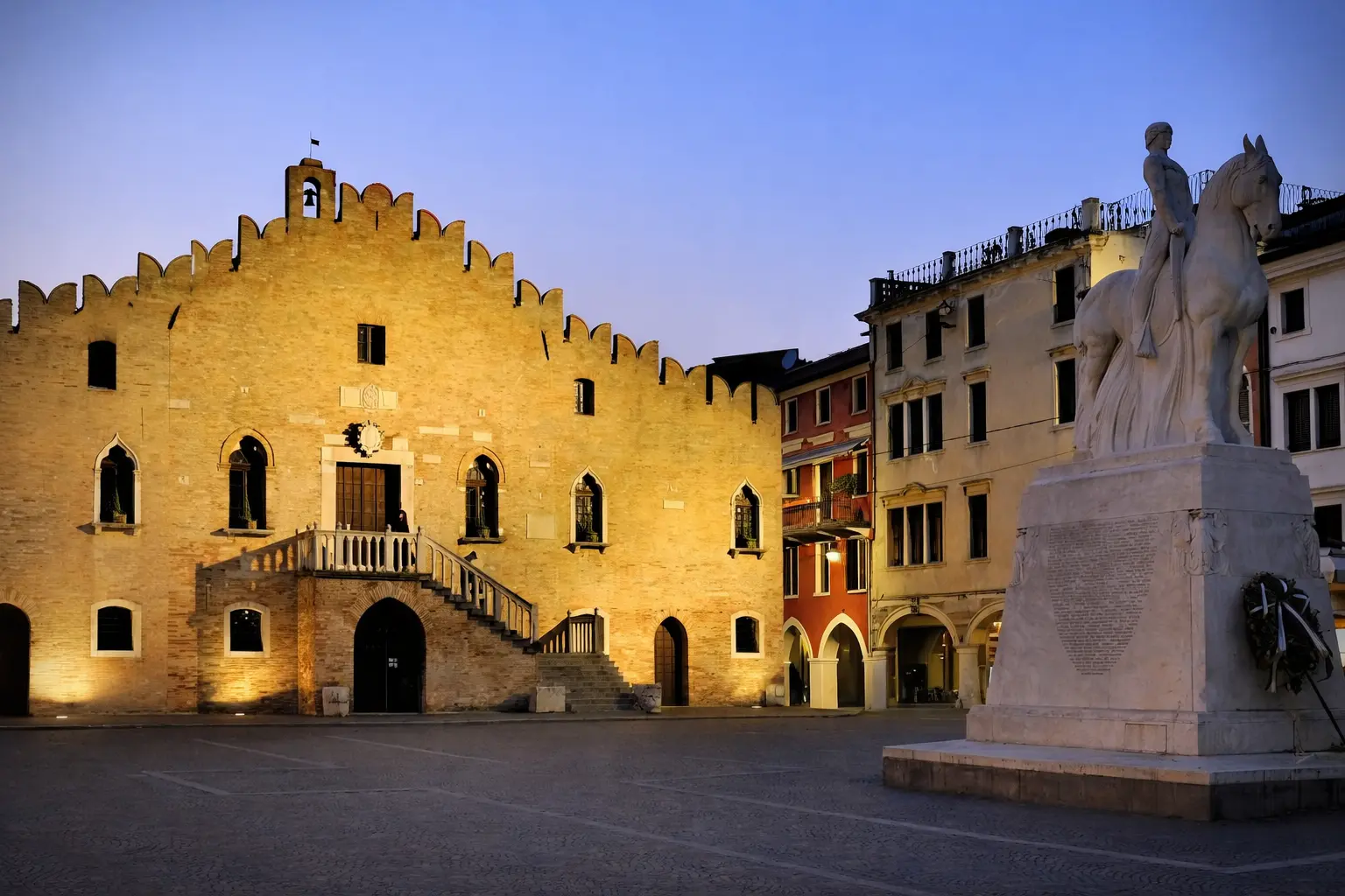Piazza italiana al crepuscolo con statua e palazzo storico.