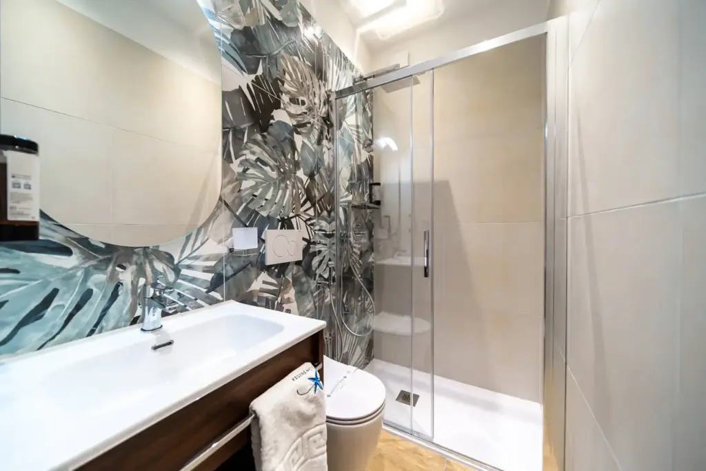 Bagno moderno con doccia e decorazioni floreali a parete.